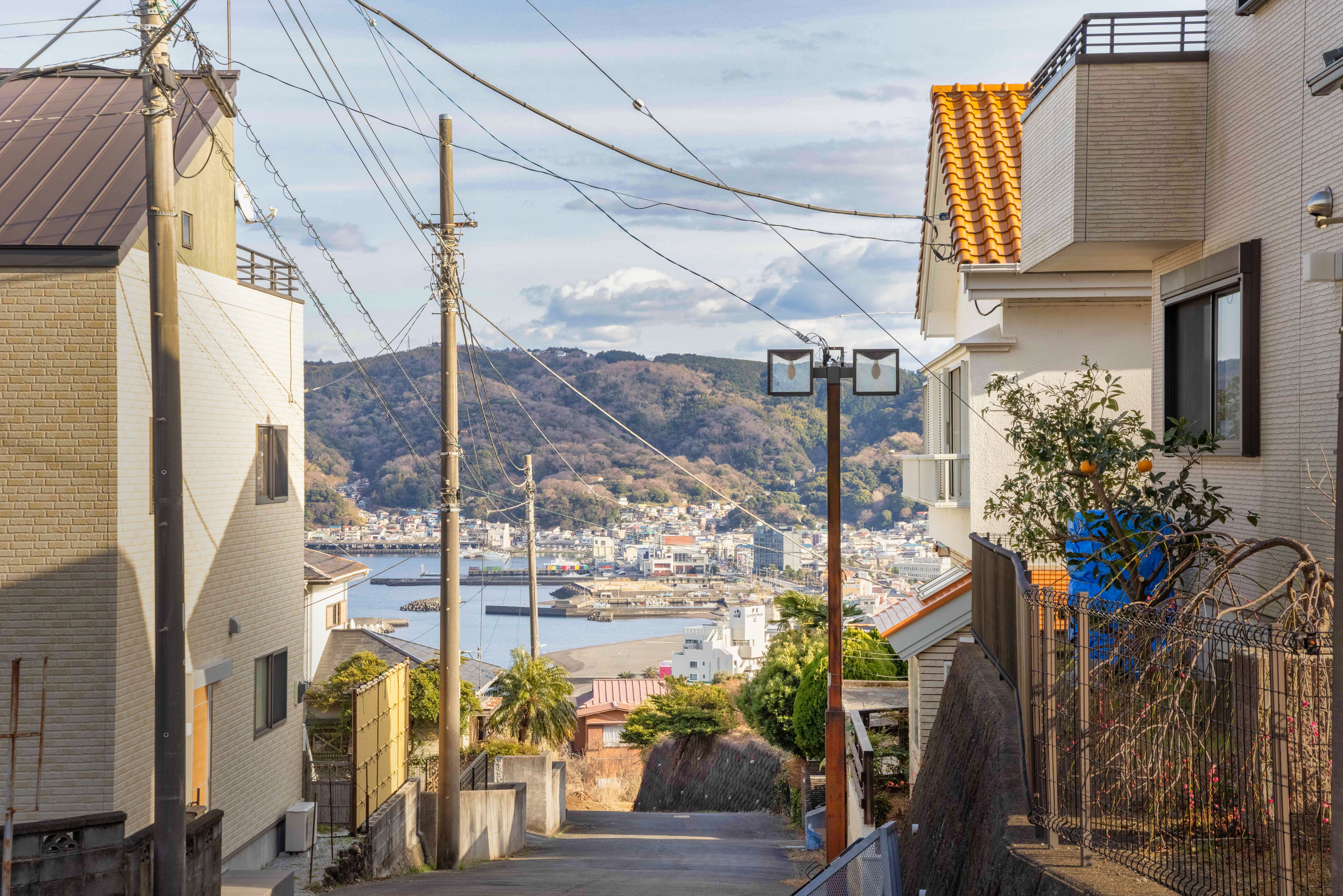 Street view with cityscape in the background, houses on both sides, power lines above, and a view of the bay and hills under a partly cloudy sky. Street view with cityscape in the background, houses on both sides, power lines above, and a view of the bay and hills under a partly cloudy sky.
