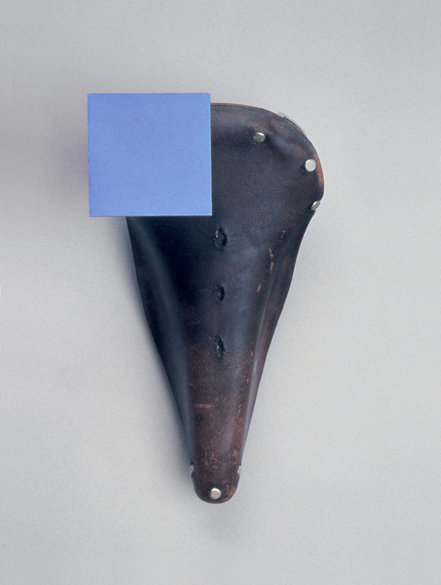 A vintage leather bicycle seat with minimalist blue square covering one corner.