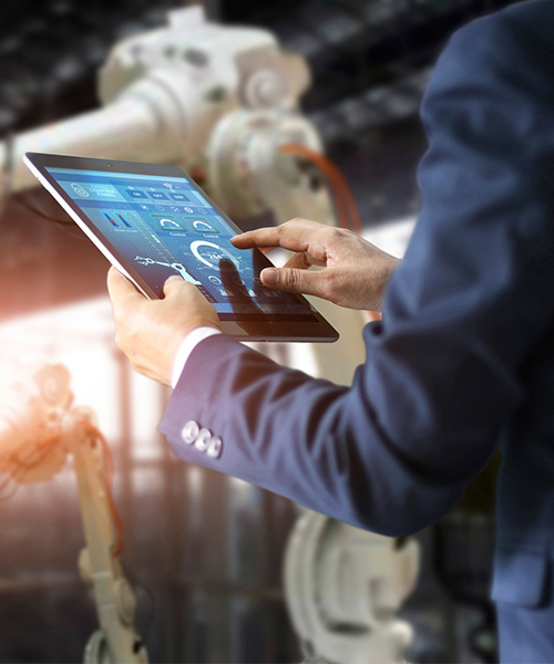 A man holding a tablet device surrounded by robot arms in a factory