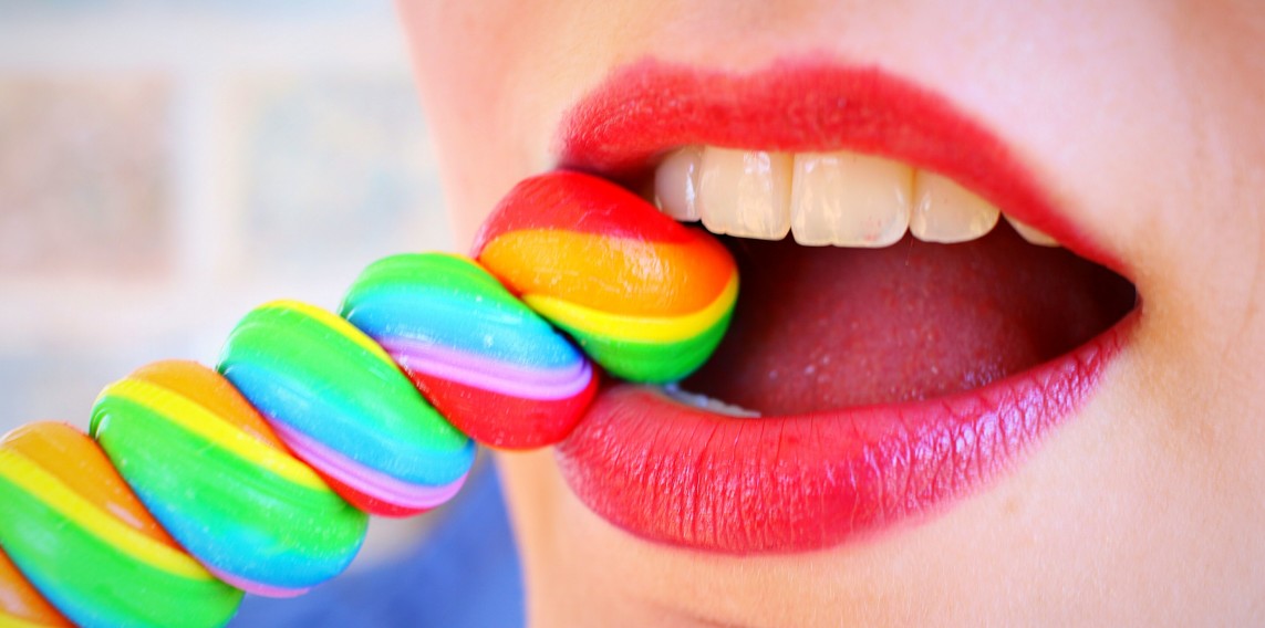 woman with pink lipstick biting rainbow-colored stick candy about to chip a tooth