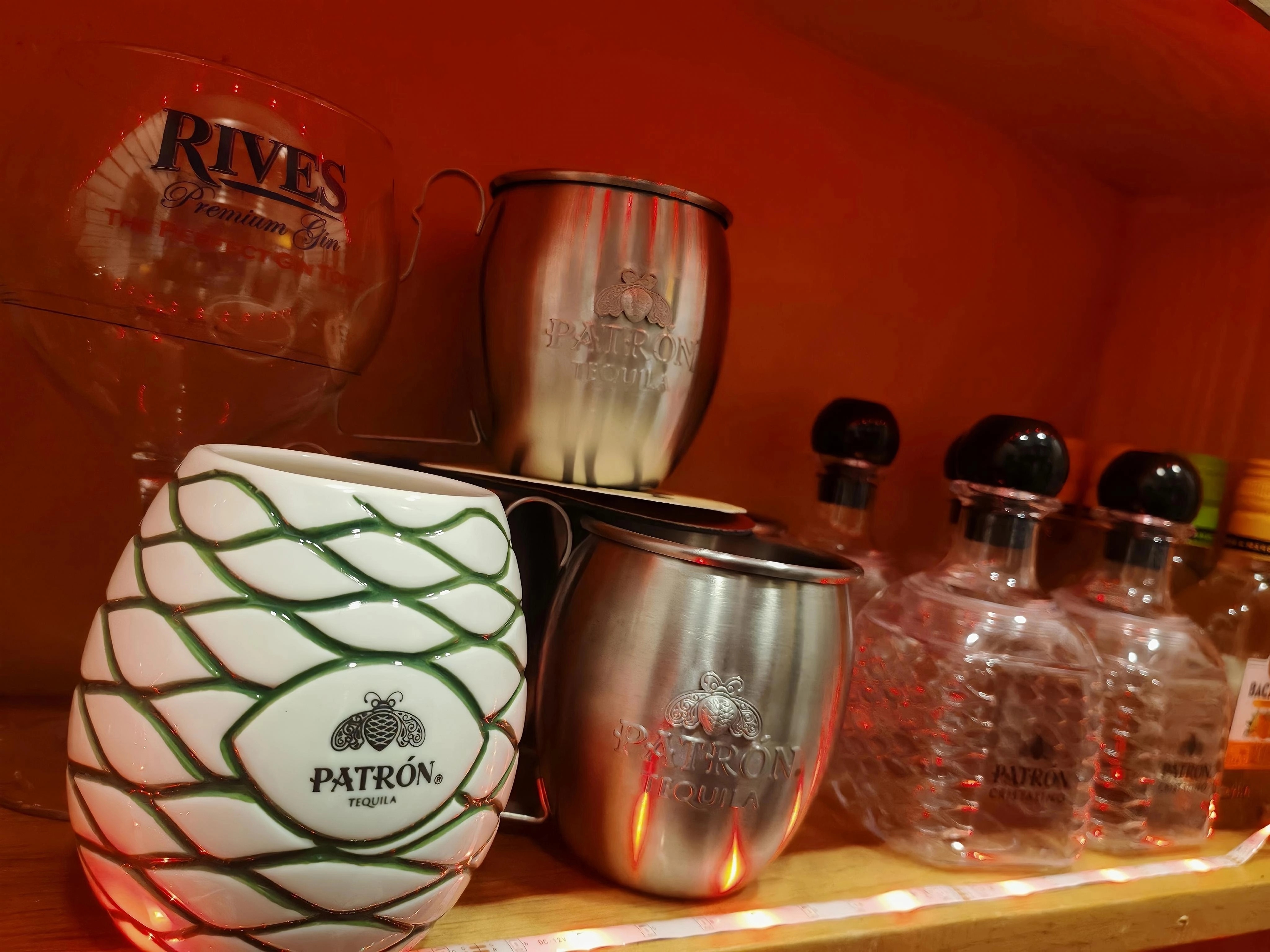 Bar moderno con taburetes y amplia selección de botellas en la barra, grandes ventanales y plantas decorativas.