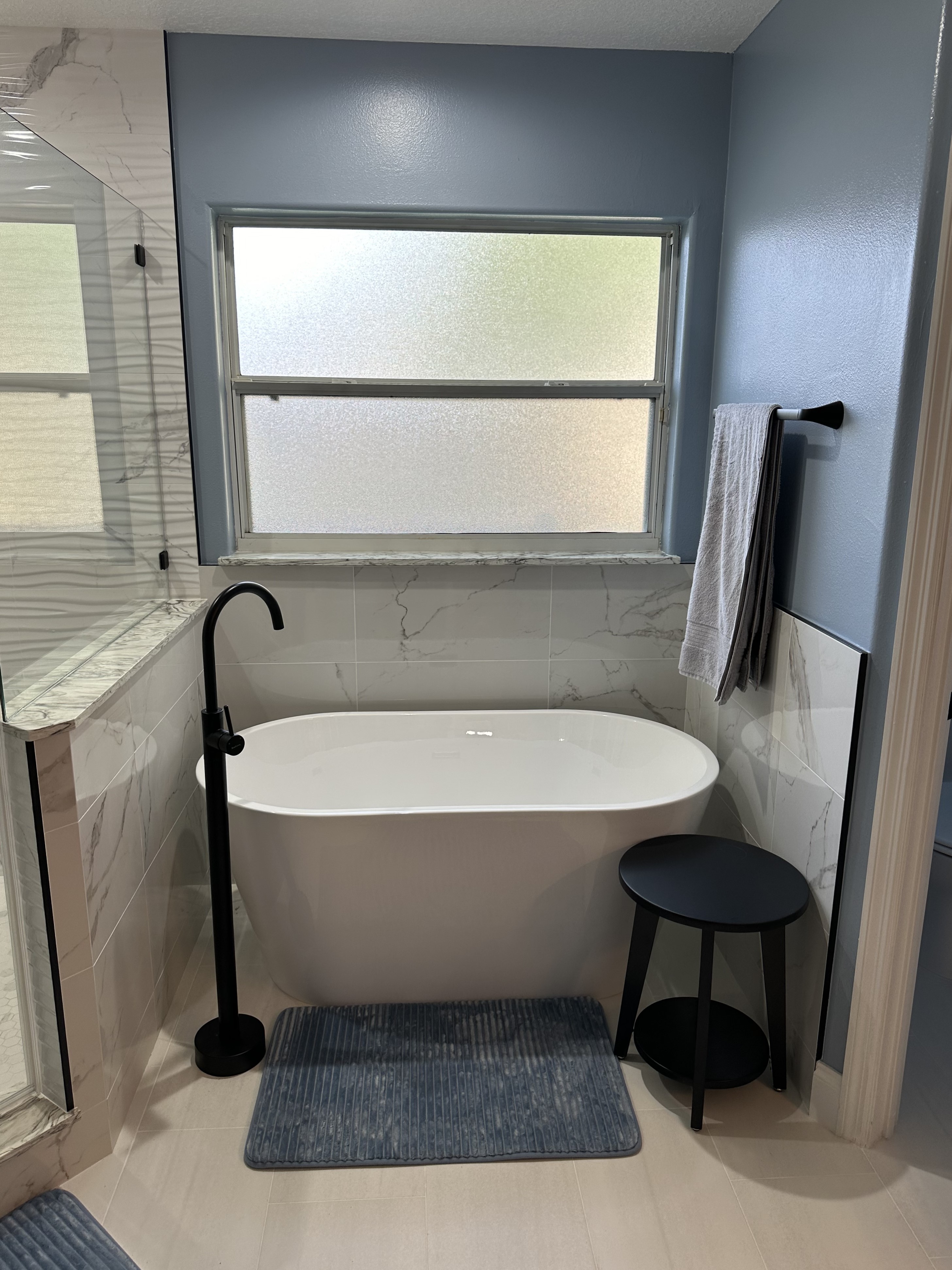 The large freestanding soaking tub with Statuario Glossy 12x24 wall tile surround and matte black freestanding tub faucet is a true spa-like retreat.