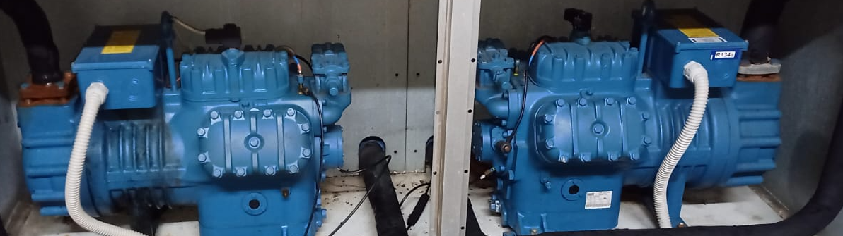 Compresores industriales azules instalados en un recinto, conectados por tuberías y cables.