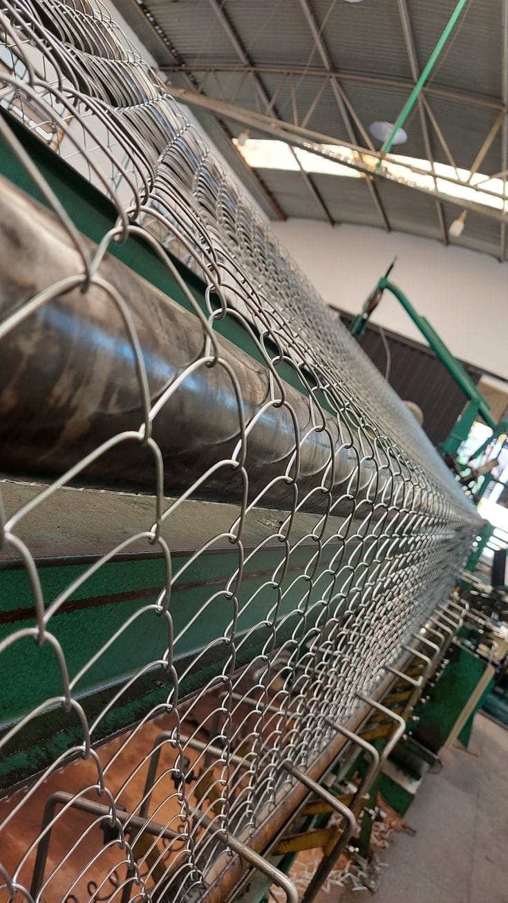 Máquina en fábrica produciendo cercas de alambre en un entorno industrial.