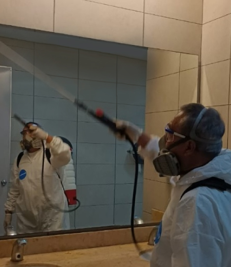 Hombre limpiando el suelo de un moderno vestíbulo con un abrillantador, rodeado de muebles y plantas grandes.