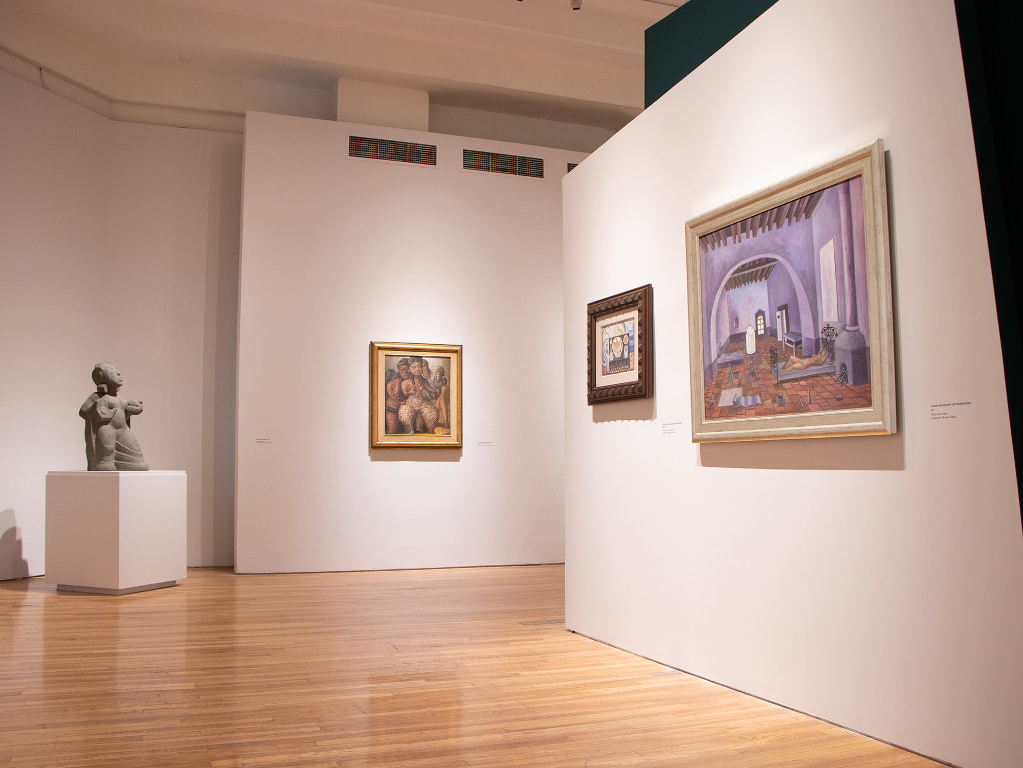 Exposición de arte con piezas de madera flotante colgadas en una galería iluminada, con alfombra roja y bancas.