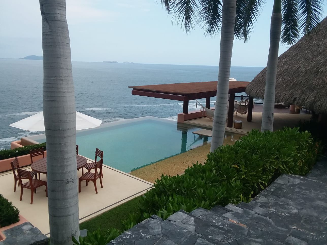 Entrada moderna de un edificio de bienes raíces con plantas decorativas y un letrero de venta de propiedades.