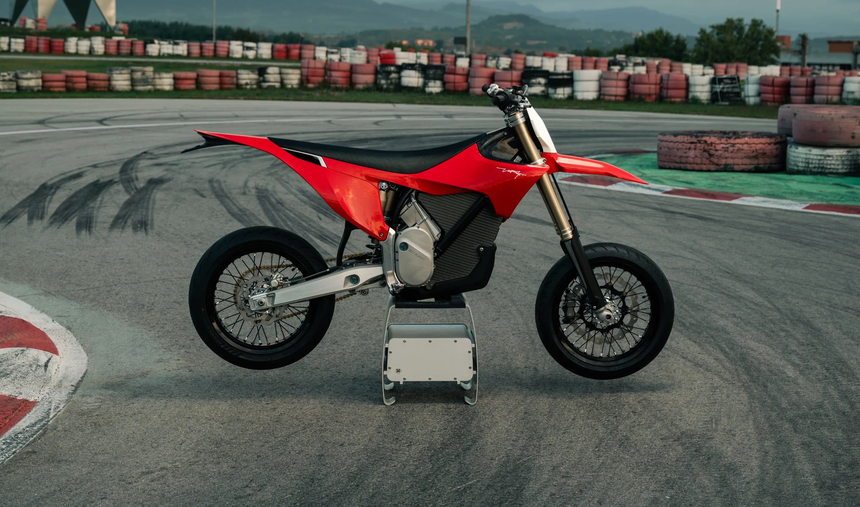 Motocicleta eléctrica roja tipo supermoto en un circuito de carreras con barreras de neumáticos
