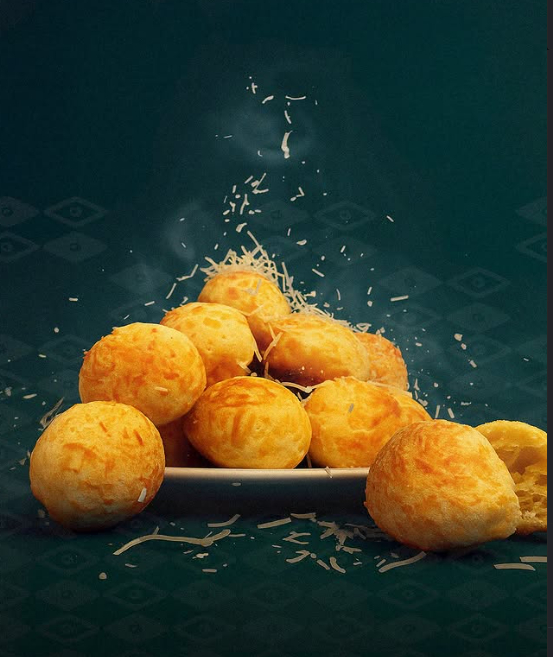 Pan de queso brasileño en plato blanco, con virutas de queso cayendo, sobre fondo verde. Pan de queso brasileño en plato blanco, con virutas de queso cayendo, sobre fondo verde.