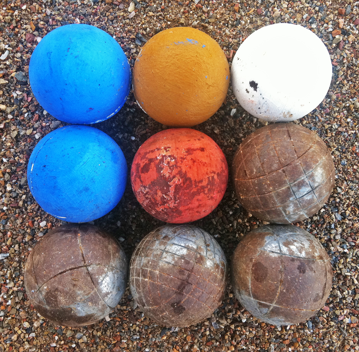 Nine bocci balls, some metal, others bright painted wood, arranged in a square.