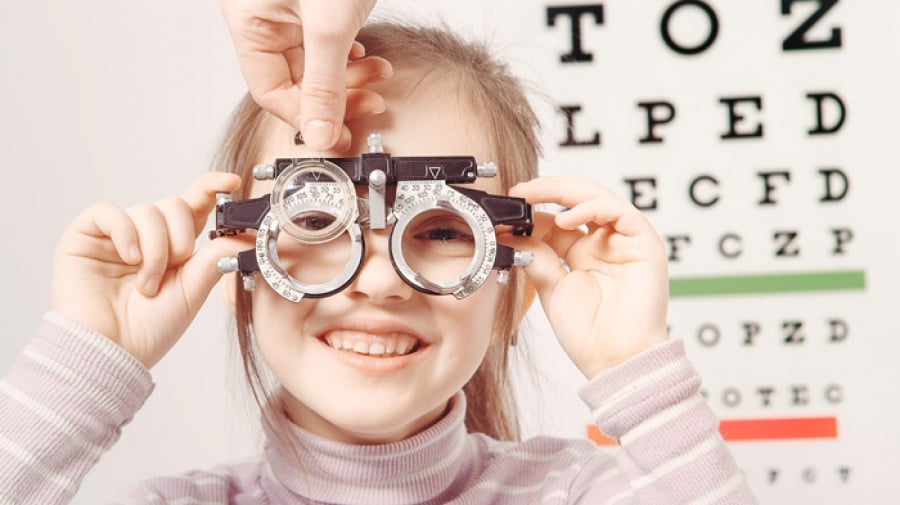 Niña sonriendo mientras se realiza un examen de la vista con un optotipo de fondo.