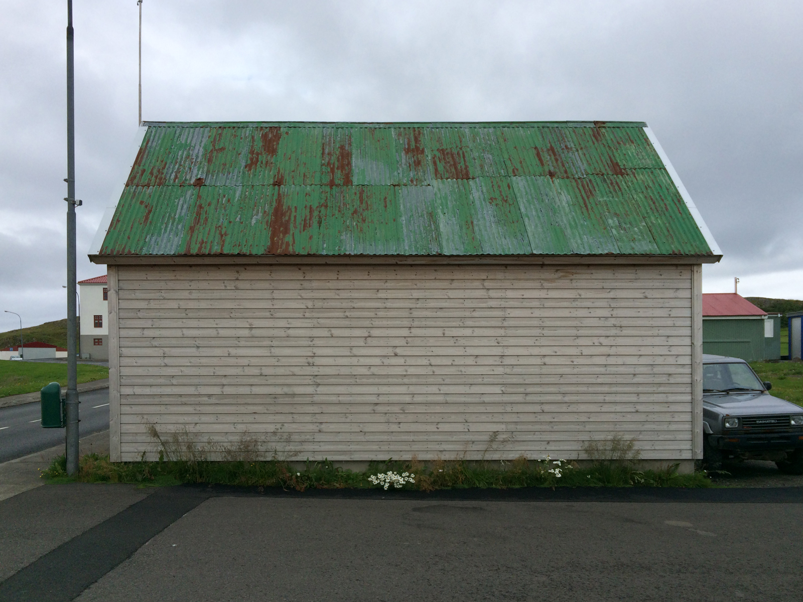 A windowless wall of a white clapboard building with a rusted green metal roof.