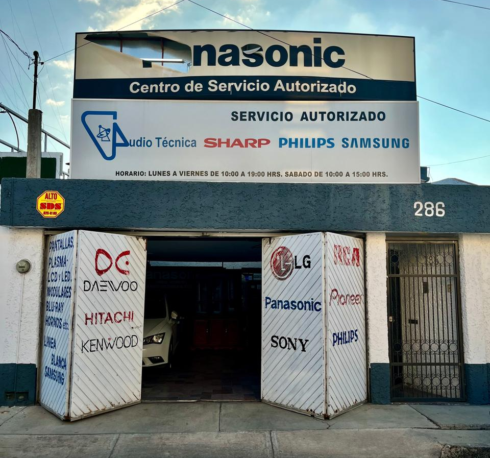 Estudio de música moderno con computadora, pantallas, altavoces y equipo de producción en una mesa blanca.