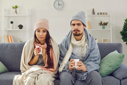 A young couple sitting inside a freezing cold home wearing multiple layers.