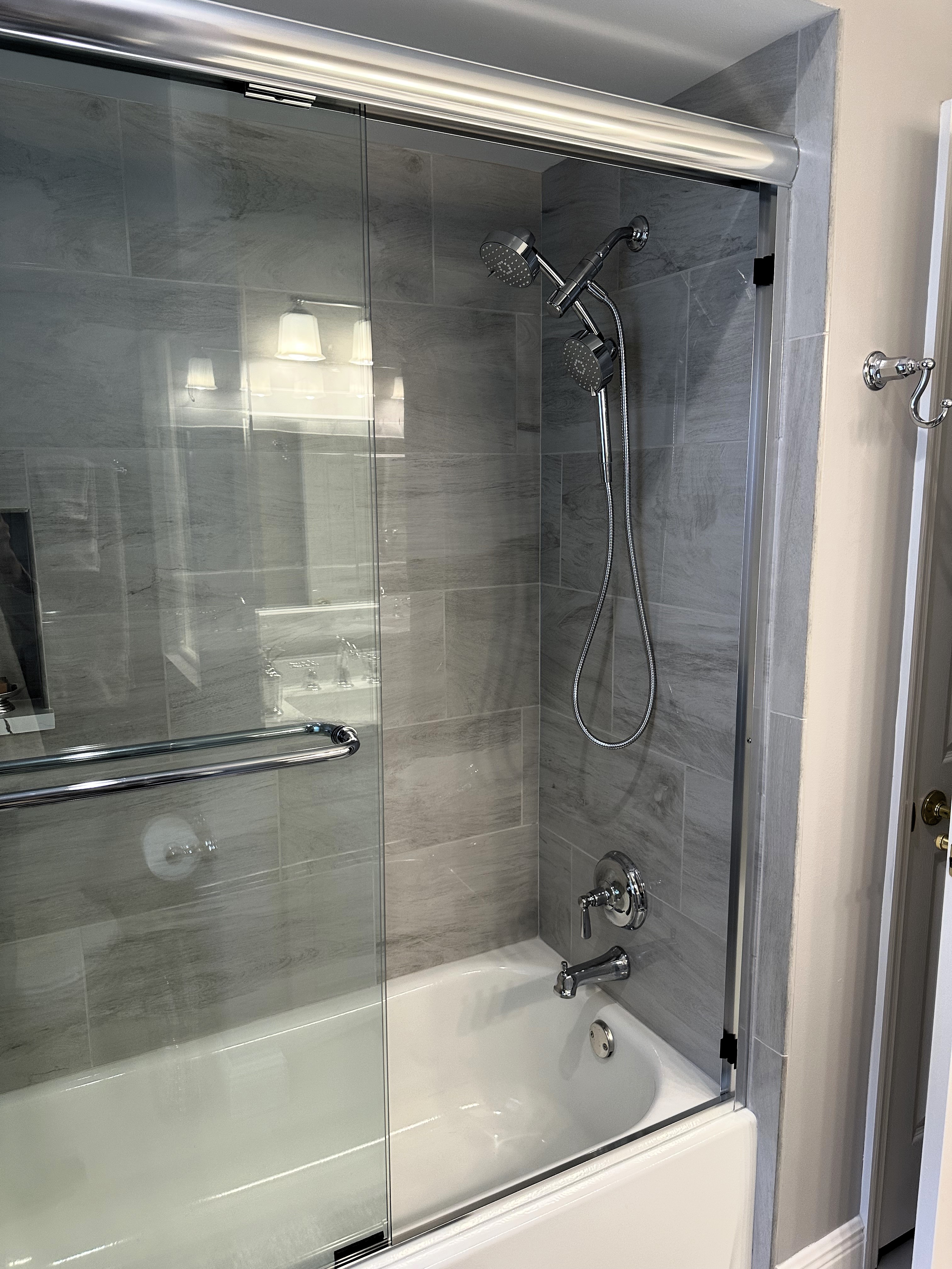 Beautiful bathroom featuring a new tub and shower with 12x24 polished wall tiles and chrome shower fixtures with clear by-passing shower doors with chrome handle and header. 