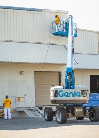 Industrial lift with workers painting a large warehouse building.