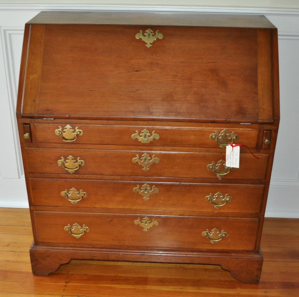 Antique wooden bureau with brass handles and multiple drawers on a hardwood floor.