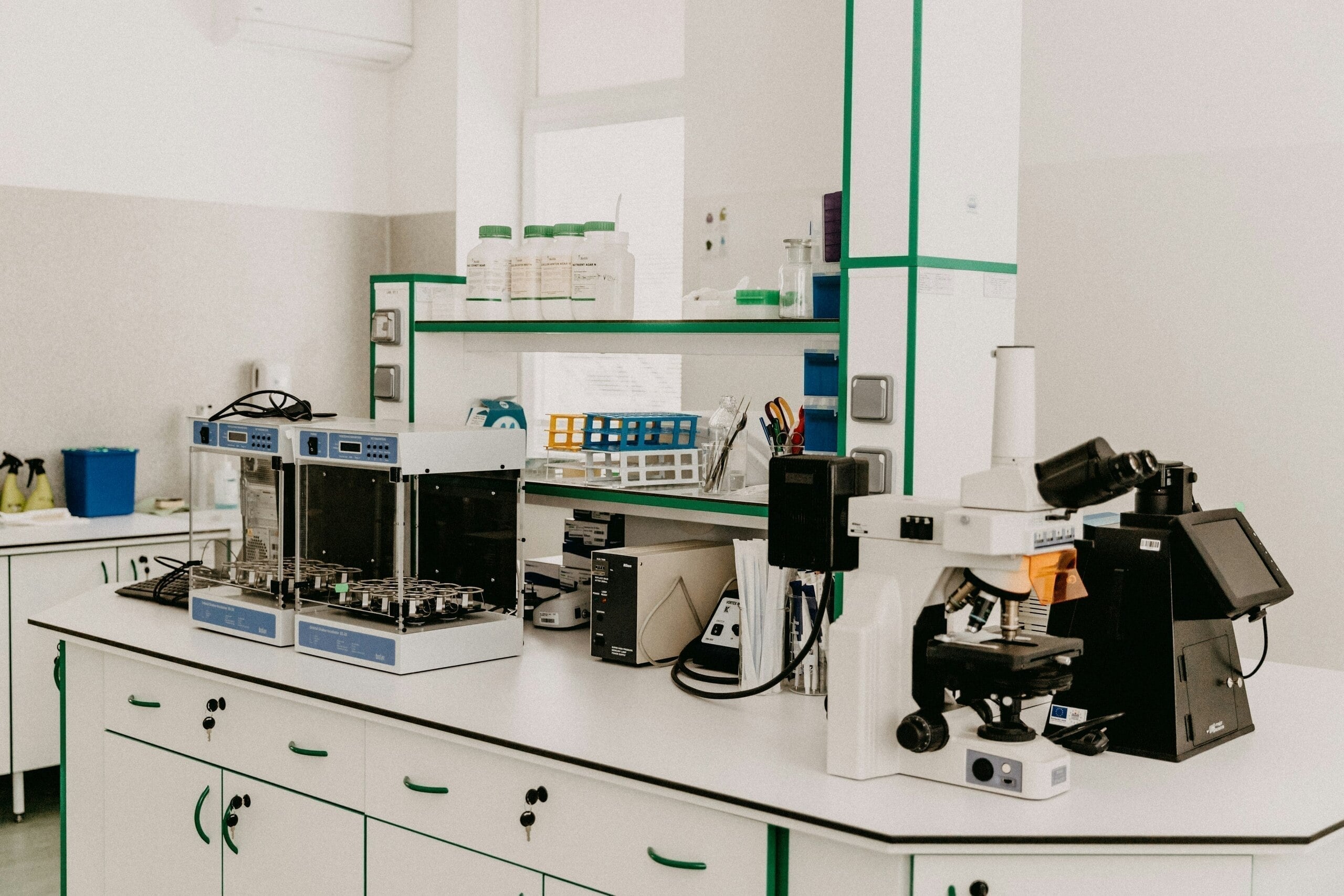 Laboratorio científico moderno con microscopio, equipos de análisis, frascos de reactivos y material de investigación sobre mesas blancas