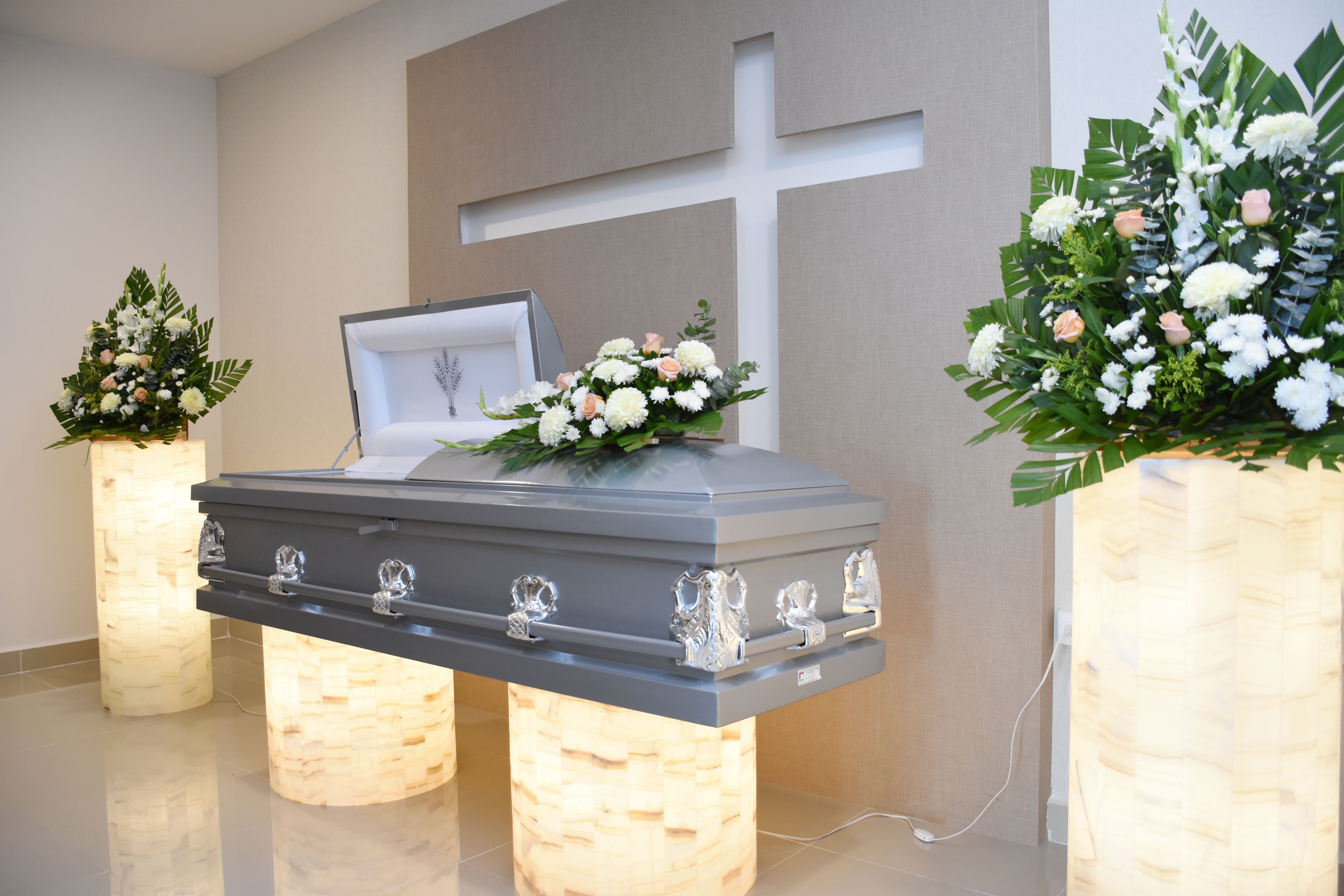 Gray casket with white and peach floral arrangements in a funeral home chapel