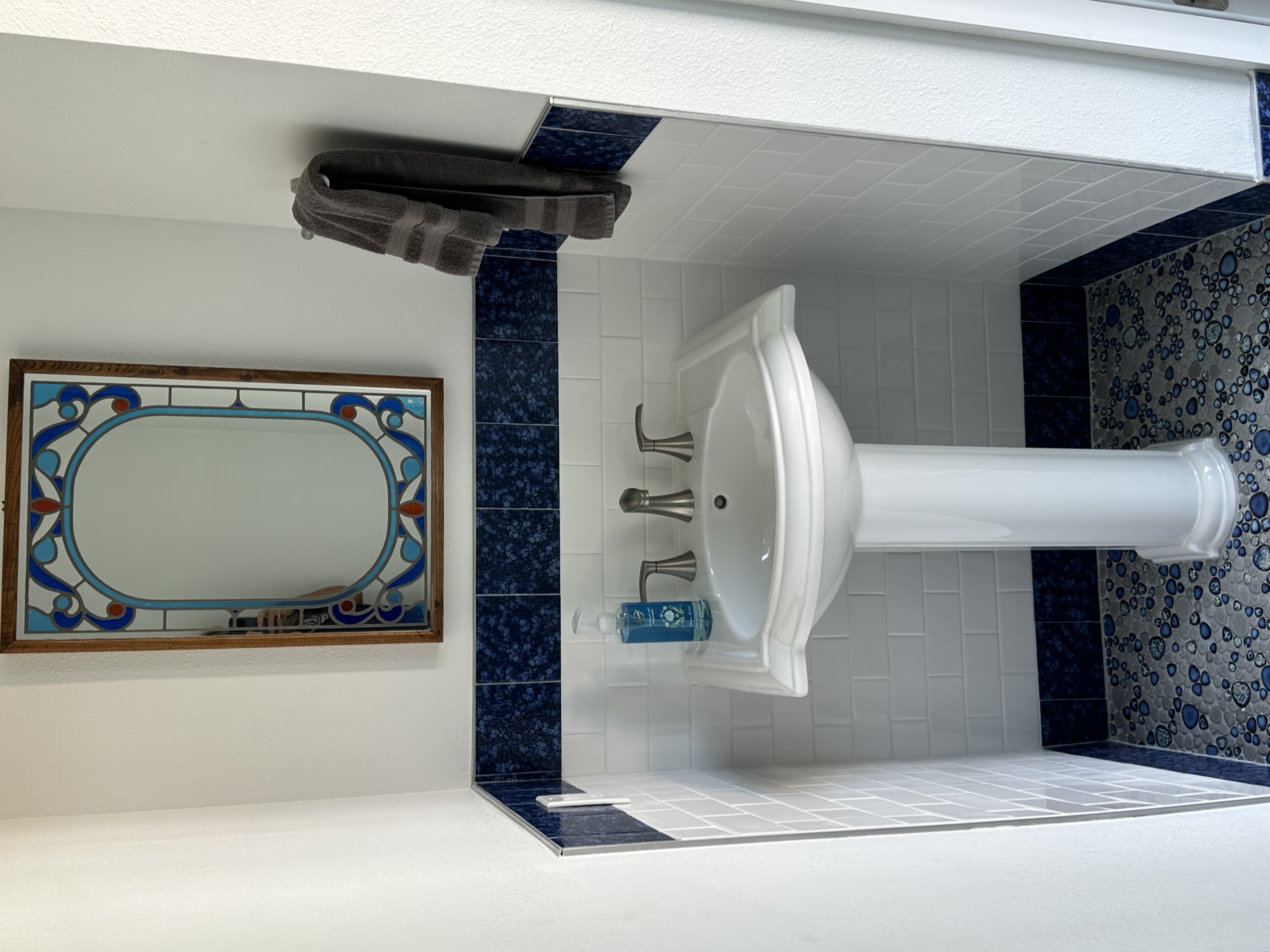 The perfect pedestal sink, paired with an adorning mirror, creates a clean and crisp space.  
The white subway tiles provide a timeless canvas, allowing the blue accents and porcelain mosaic floor to pop.