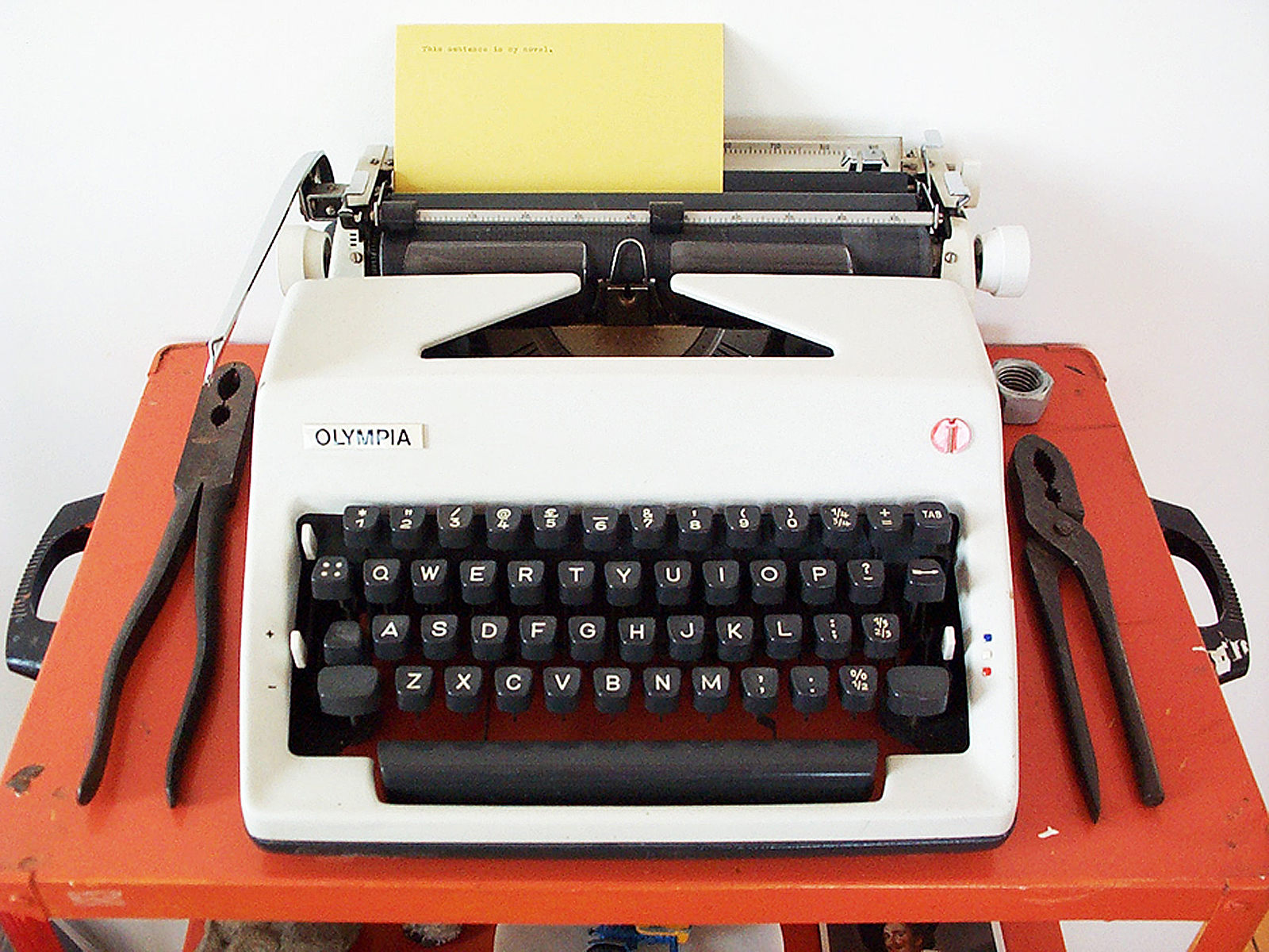 An Olympia typewriter with typed card and two pairs of pliers on an orange cart.