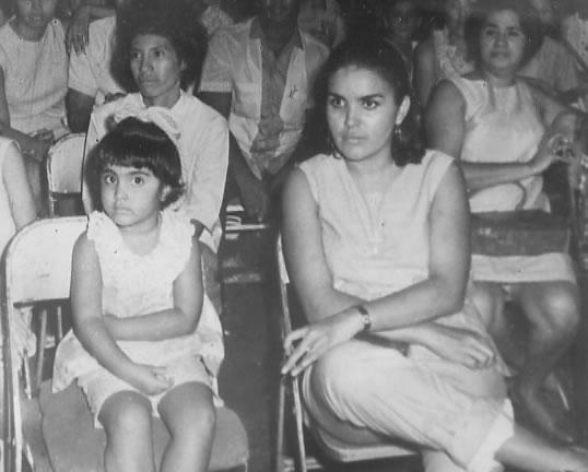 Esta foto define mi relación con mi madre. Fue tomada una tarde de domingo en el circo. Mi madre sabía lo mucho que me encantaba el circo, y a pesar de que llovía torrecialmente, cumplió su promesa de llevarme. Cuando salimos,  tuvo que doblarse la basta de los pantalones para no mojarlos. Siempre fuimos las mejores amigas.