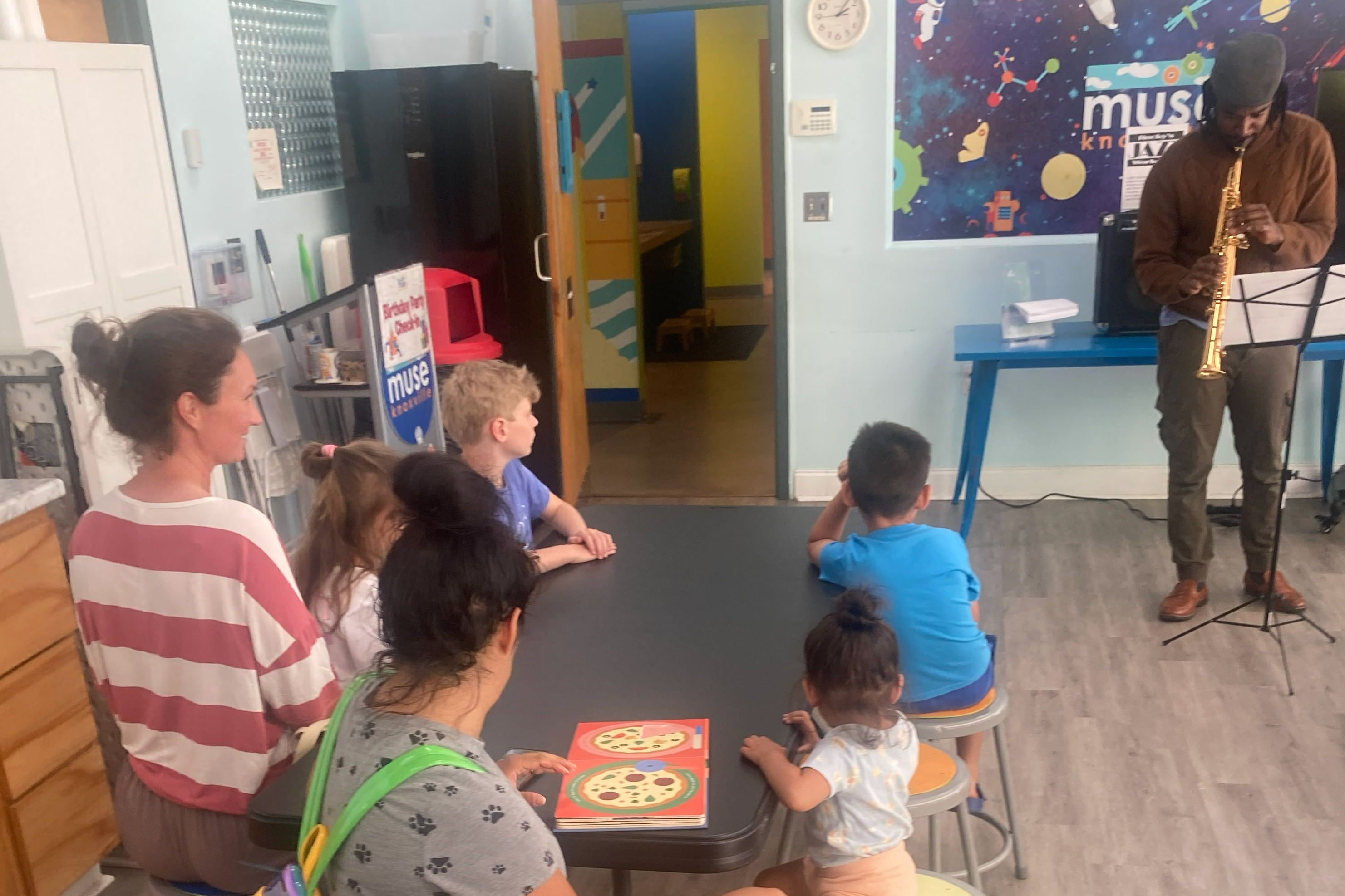 Modern music studio with piano, violin, electric guitars, and digital keyboard, featuring illuminated sheet music screens.