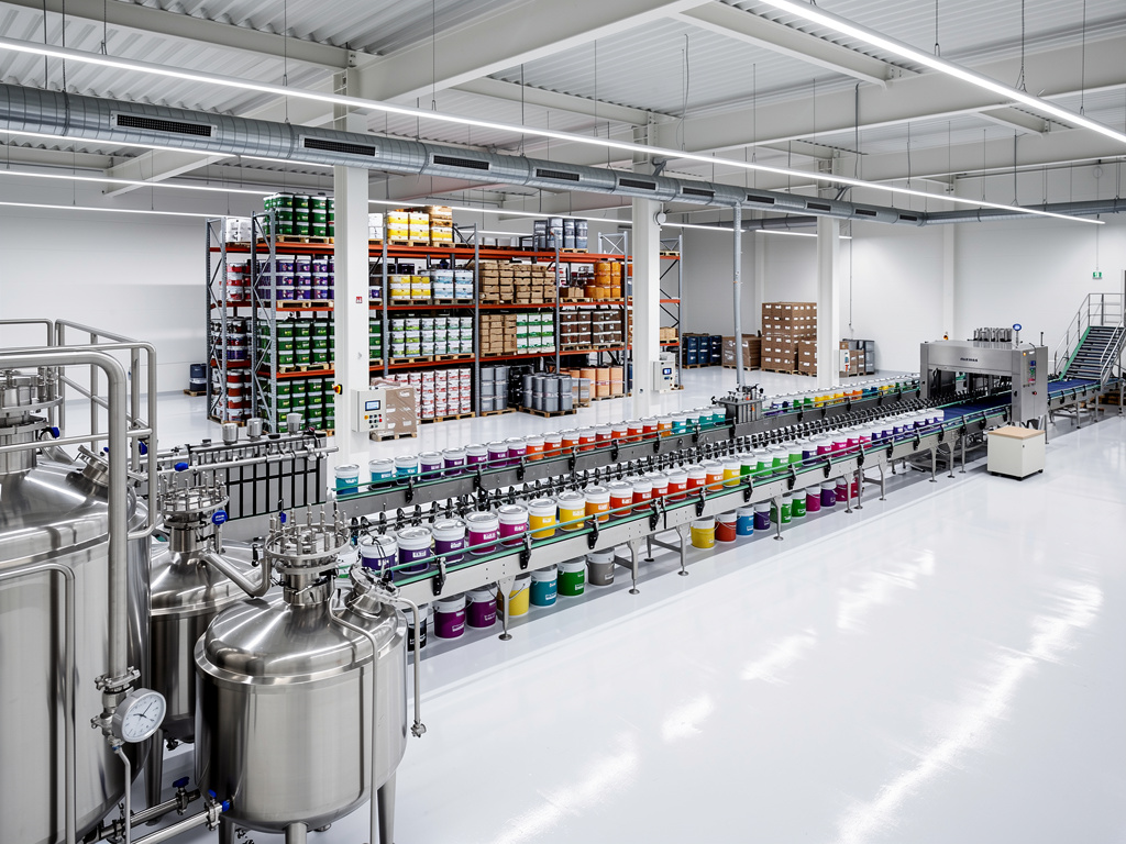 Línea de producción automatizada en fábrica de pintura con cubos de colores, tanques industriales y estanterías de almacenamiento