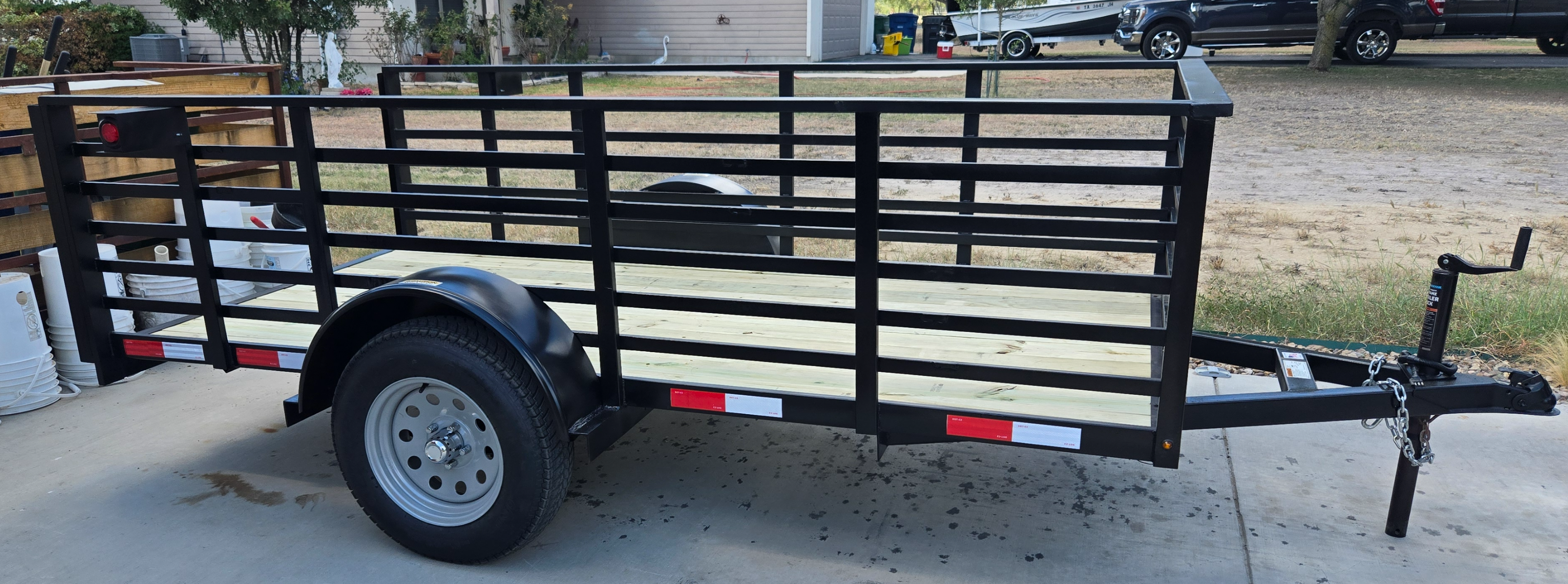 Flatbed utility trailer parked on a driveway in front of a row of storage garage doors.