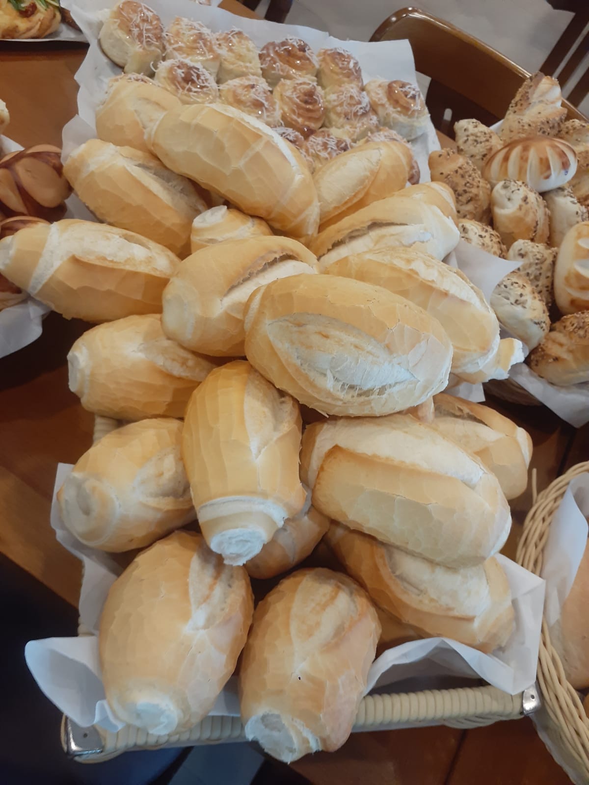 Cesta de pães frescos e variados em uma padaria, incluindo pães franceses e pães doces decorados.