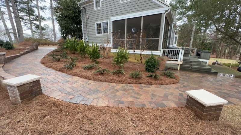 Charming brick house with dormer windows and a lush, colorful garden featuring a stone pathway under a clear blue sky.