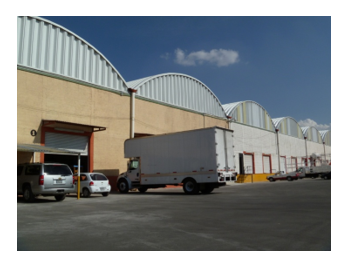 Fachada de almacén industrial con camiones y coches estacionados en un día soleado Fachada de almacén industrial con camiones y coches estacionados en un día soleado