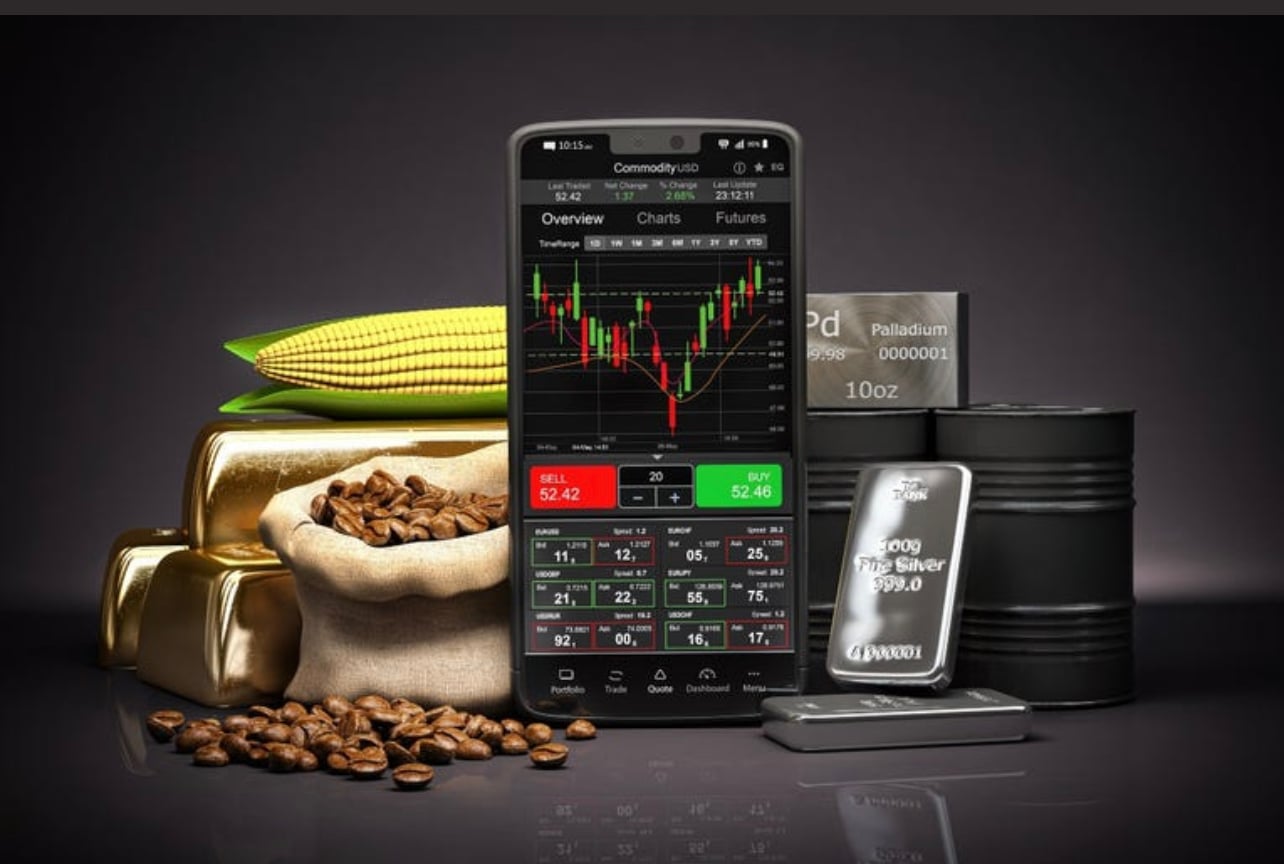 Smartphone displaying commodity trading app with charts, surrounded by gold bars, corn, coffee beans, silver bars, and oil barrels. Smartphone displaying commodity trading app with charts, surrounded by gold bars, corn, coffee beans, silver bars, and oil barrels.