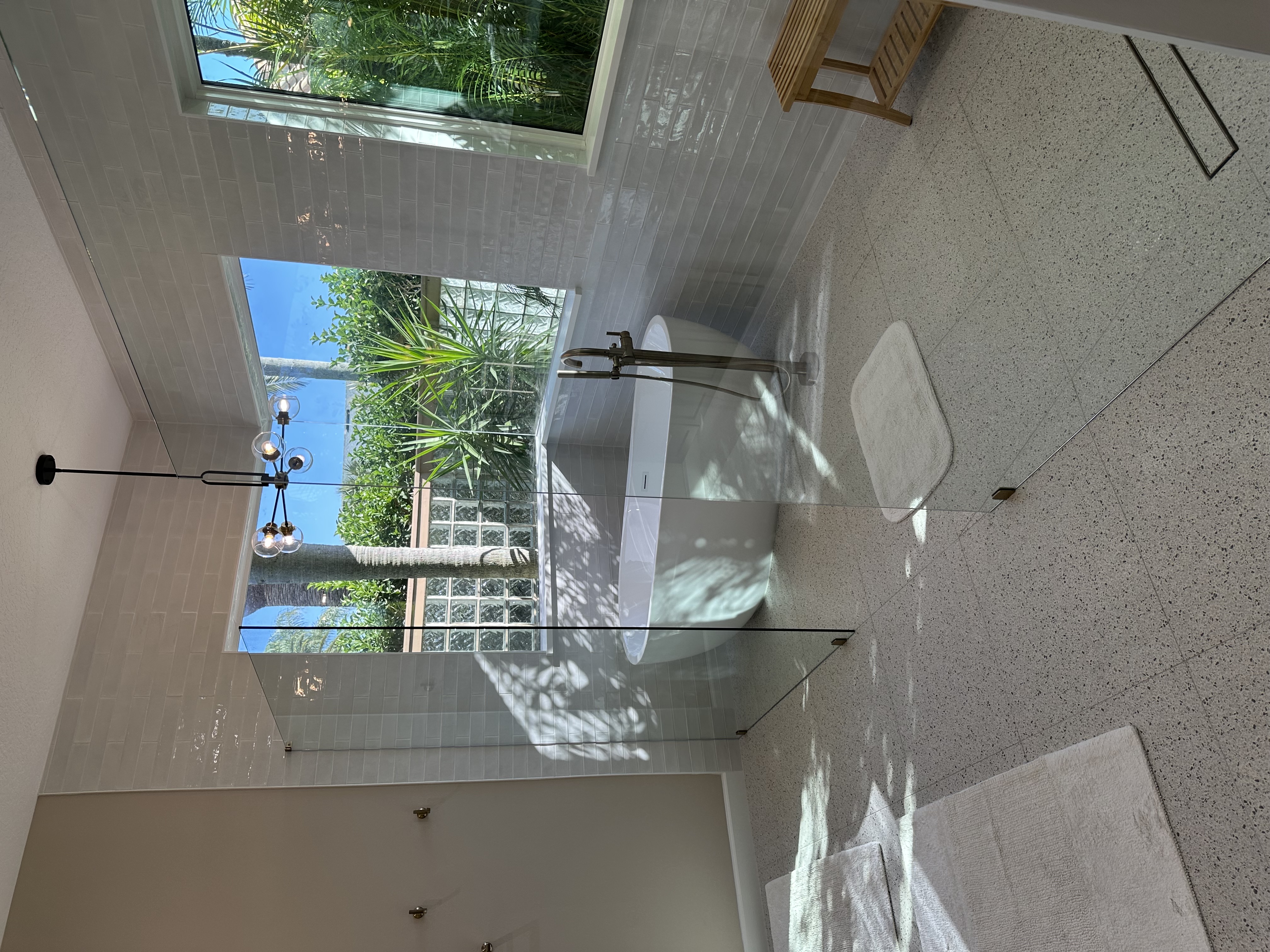 Large 24×24 square floor tiles create a serene, spa-like retreat, featuring a freestanding tub,
luminous white glossy tile surround, and sleek 3/8″ clear glass.