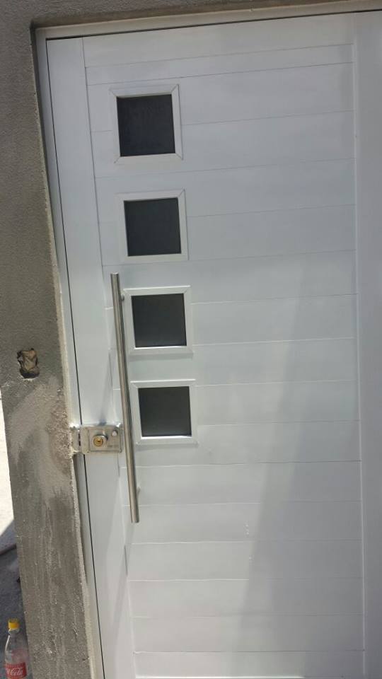 Puerta de aluminio con duela lisa tono blanco, con detalle de cristales a los lados, jaladera tipo H y chapa de seguridad.