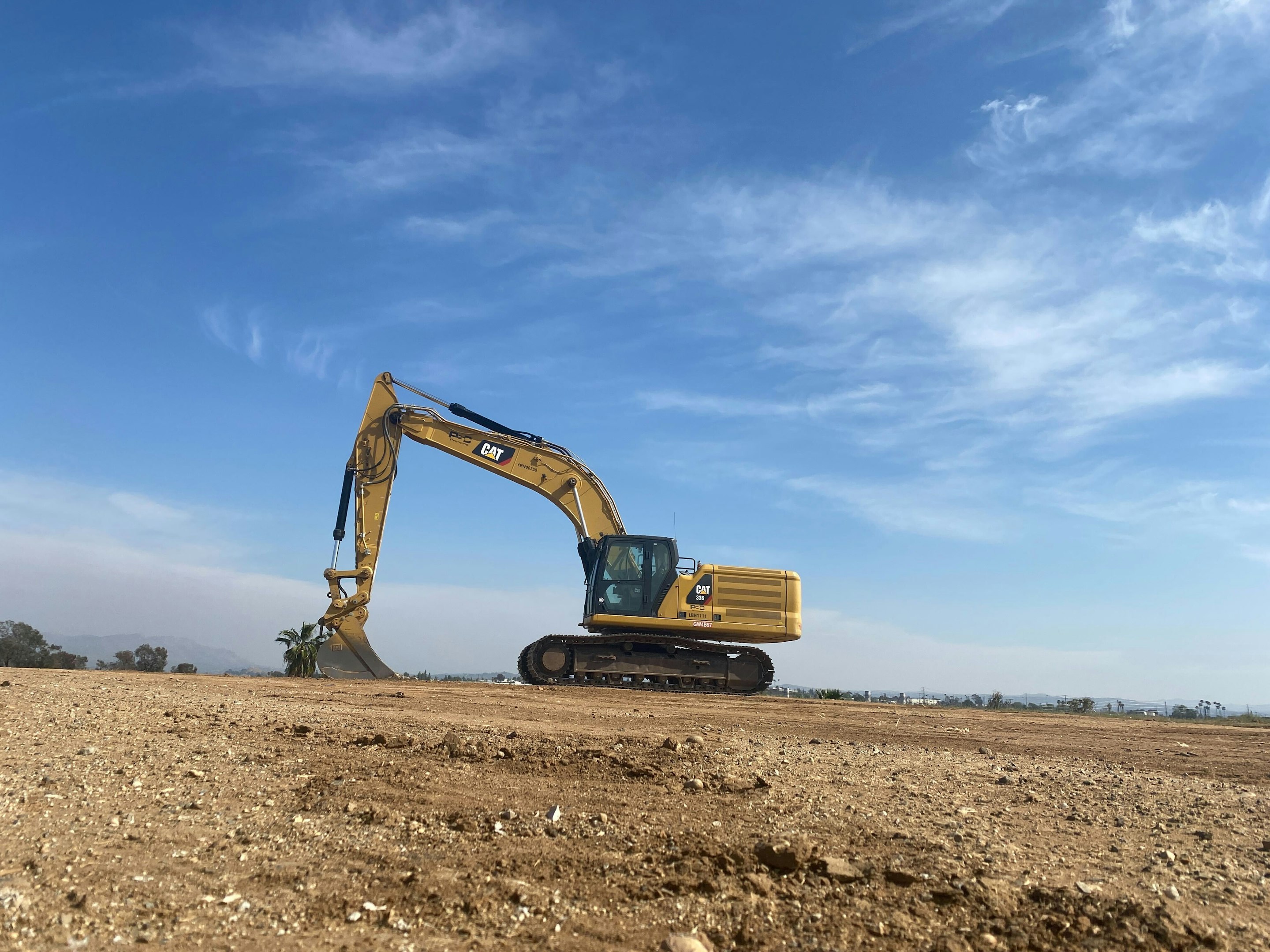 an excavator on a dirt field under a blue sky an excavator on a dirt field under a blue sky