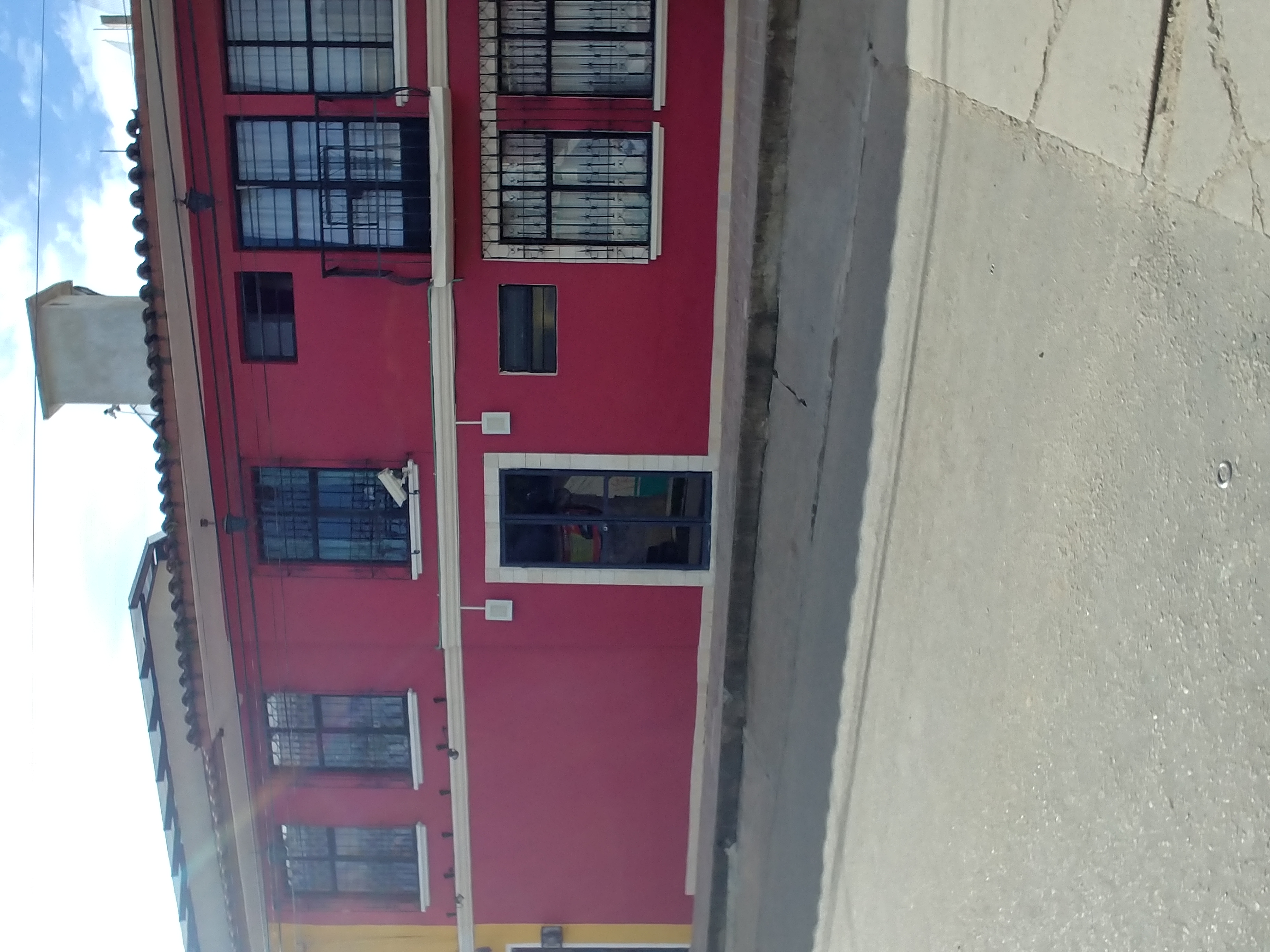 Fachada de edificio rojo con ventanas enrejadas, techo de tejas y calle urbana soleada