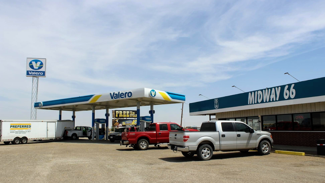 Row of RV trailers parked at a wooded campsite with picnic tables and green grass on a sunny day.