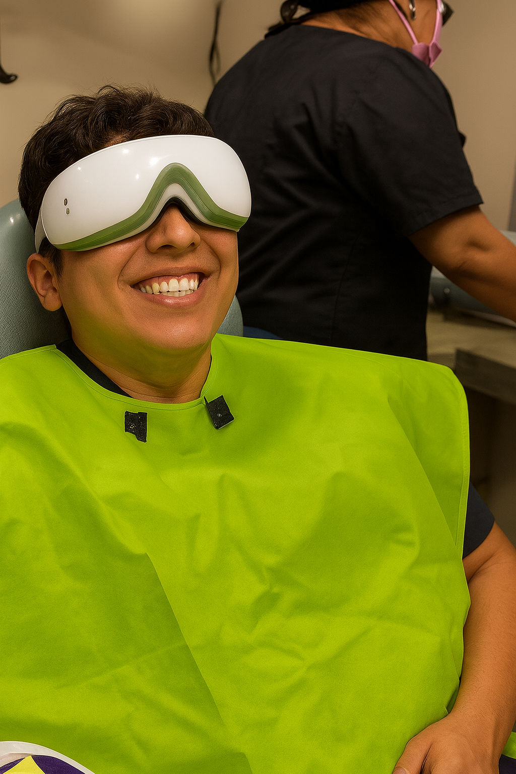 Persona sonriendo en una clínica dental con gafas de protección y delantal verde.