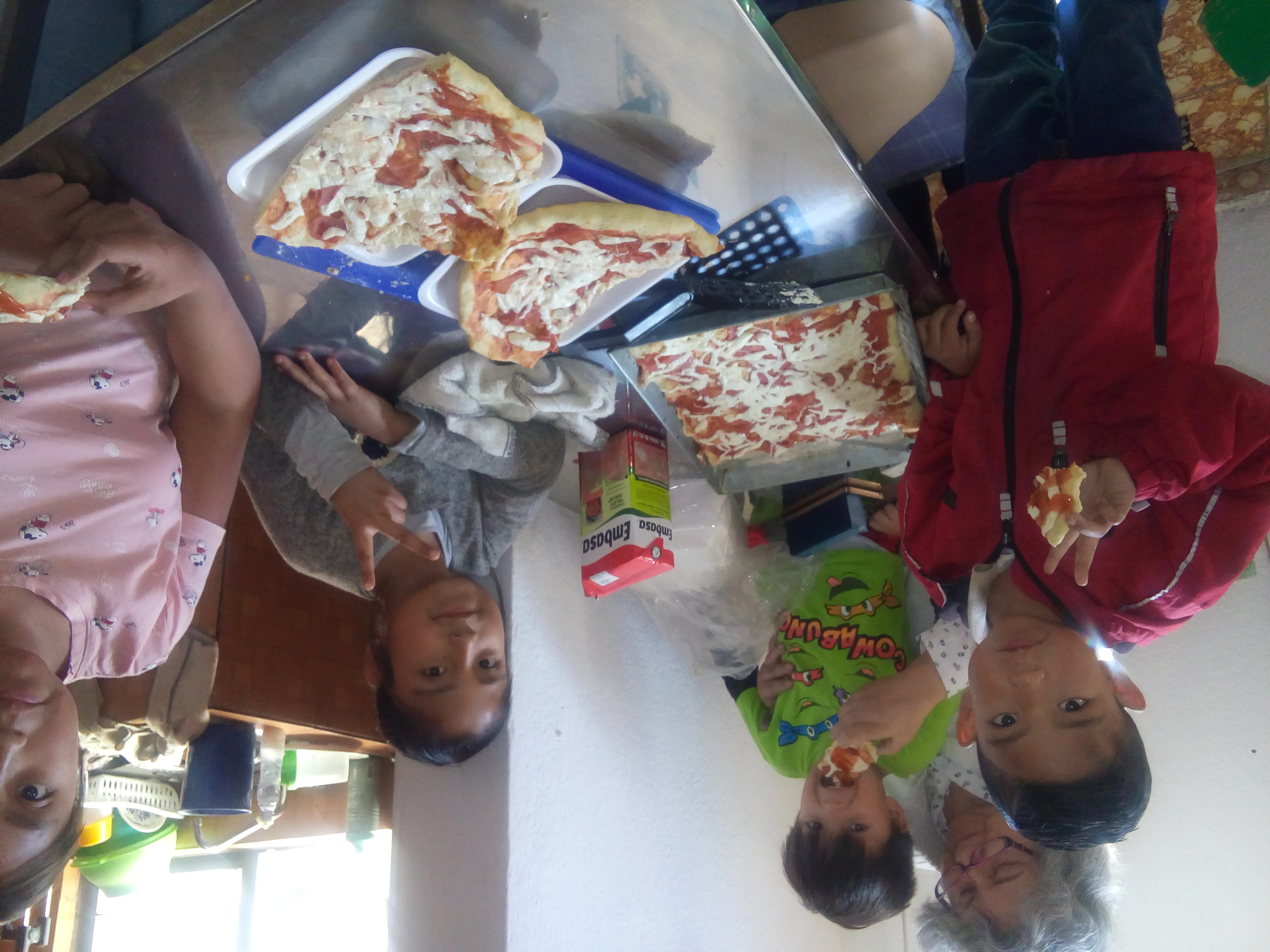 Niños disfrutando de pizza casera alrededor de una mesa con una caja de puré de tomate de fondo.