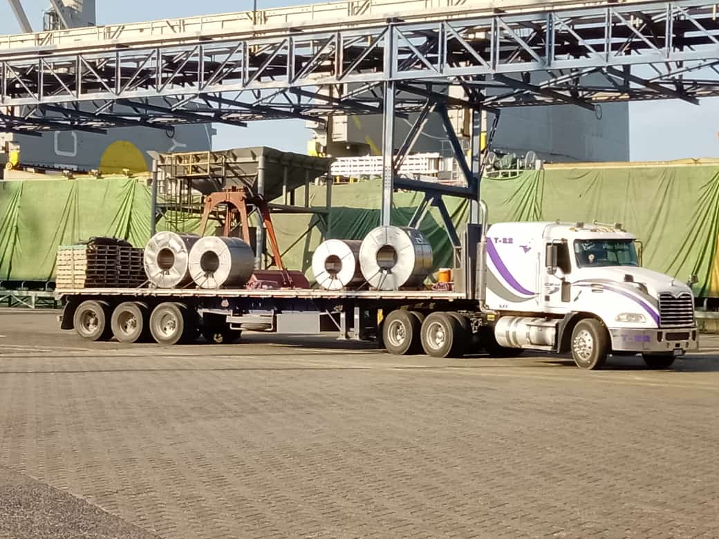 Camión blanco en almacén amplio con cajas y techo de vigas expuestas.