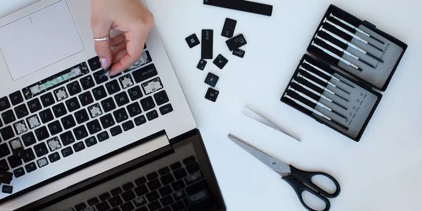 Mano reparando teclado de computadora portátil con destornilladores, tijeras y pinzas en mesa.