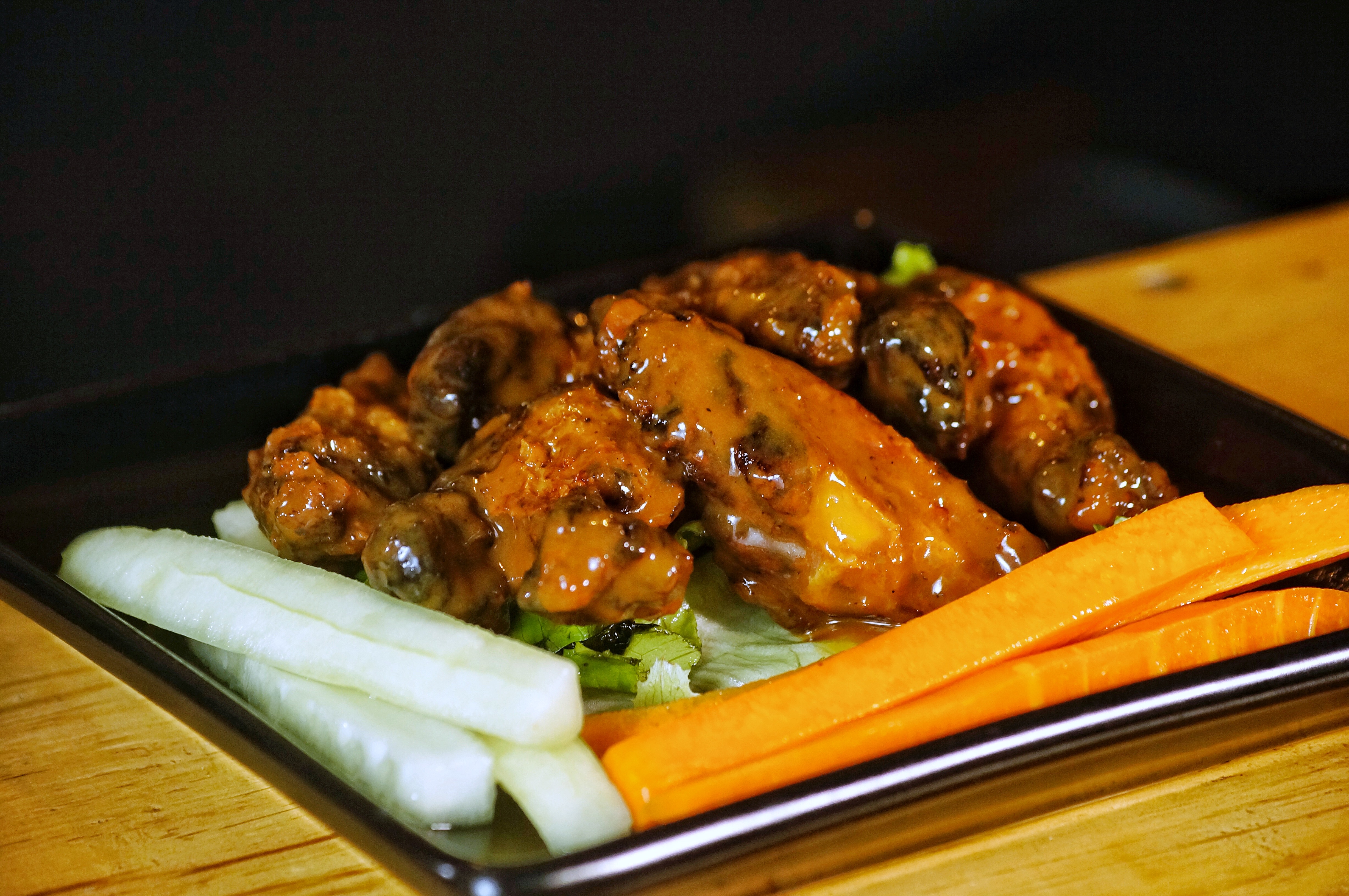 Plate of spicy buffalo wings with carrot and celery sticks on a black tray.