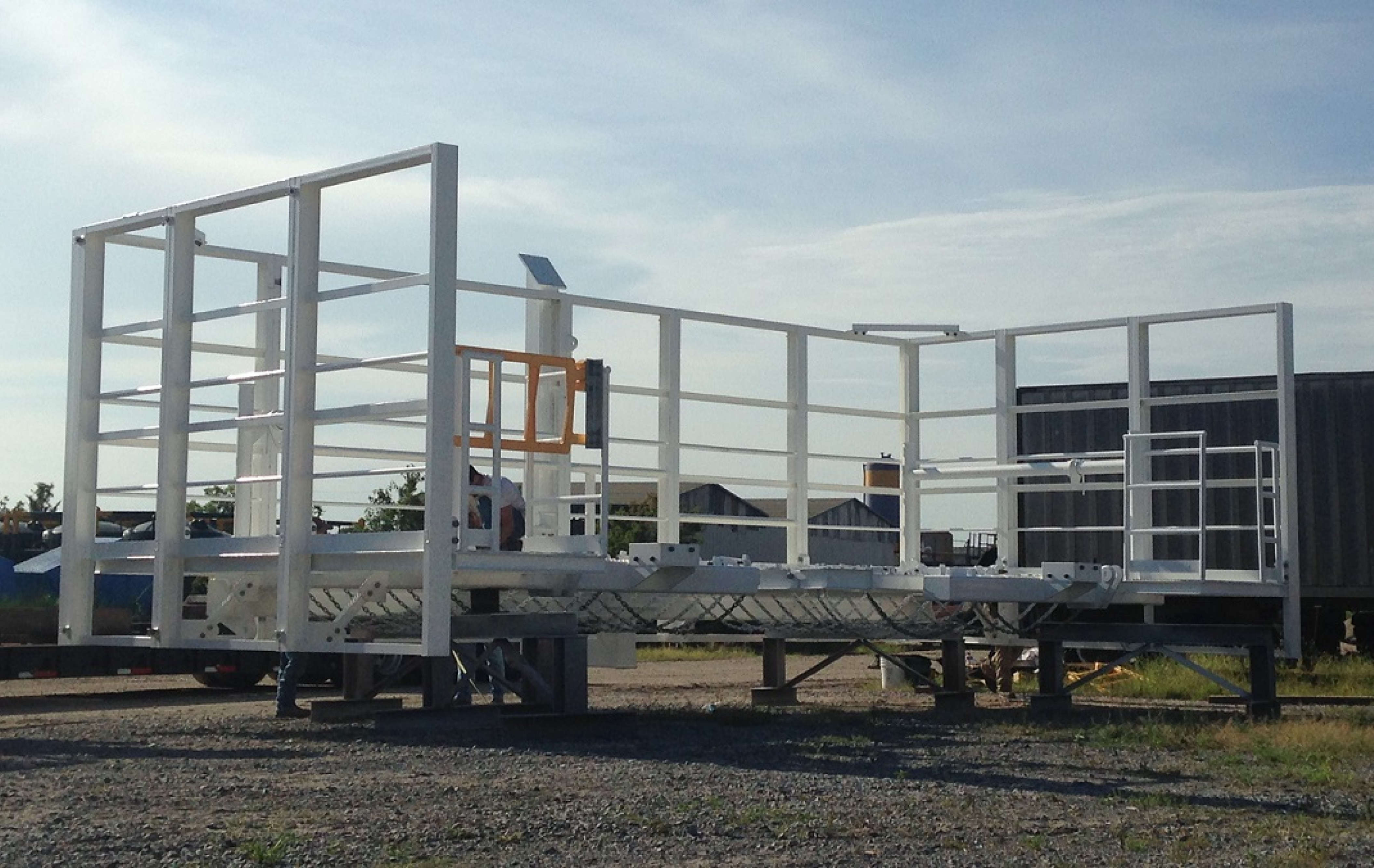 Industrial metal structures with yellow guardrails in a construction yard under a cloudy blue sky.