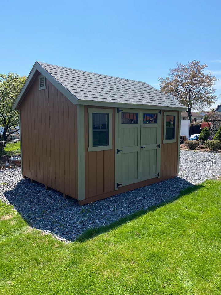 10 x 12 New England Deluxe Cape Cod In Wood                                                   
                                                             
Featuring chestnut colored wood siding, Clay colored trim, and charcoal gray colored 30 year architectural shingles (with tarpaper underlayment).
Standard features  include 4’6” wide New England doors with Deluxe hinges, 2- 18”x27” slider windows with screens, classic gable vents, and all my structures come with a 10 year warranty of materials and workmanship.

Featured Options include indoor transom Windows.