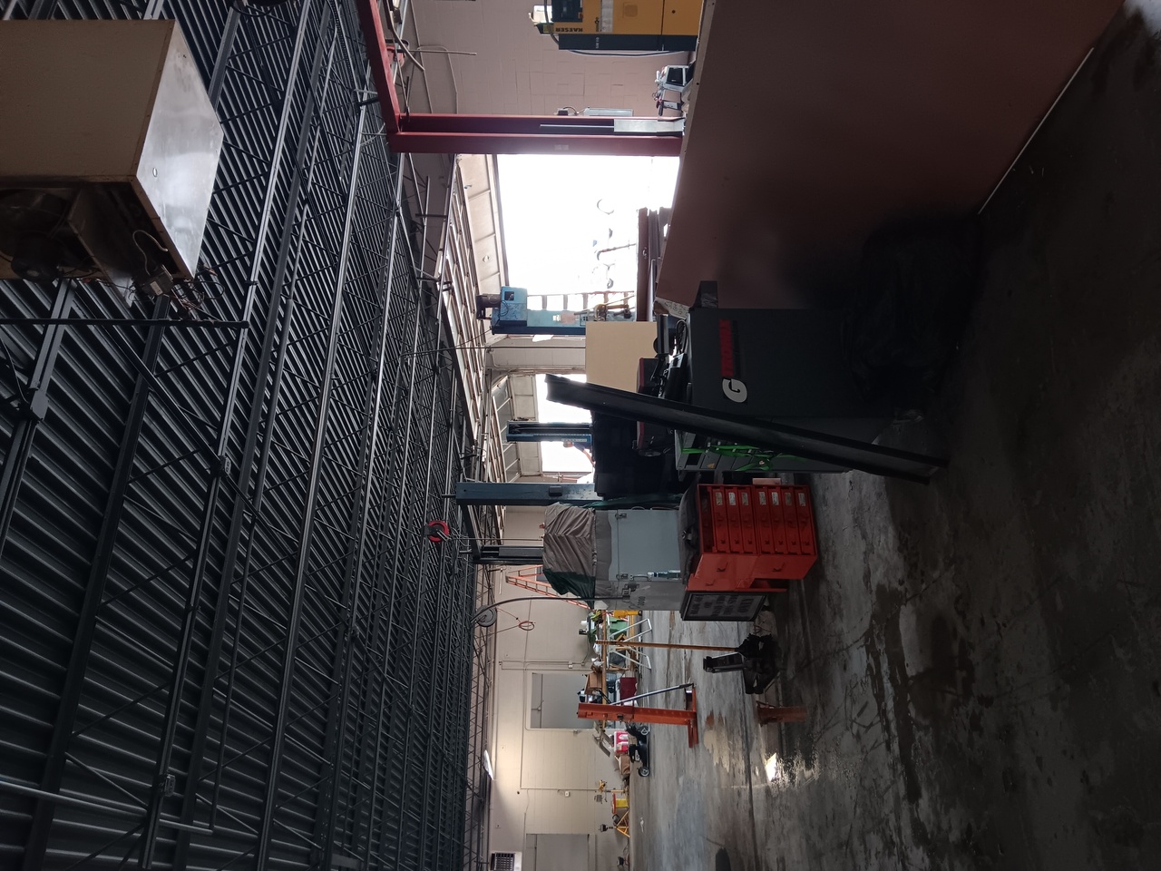 Interior of an industrial workshop with metallic ceiling, equipment, and tools scattered on the floor.
