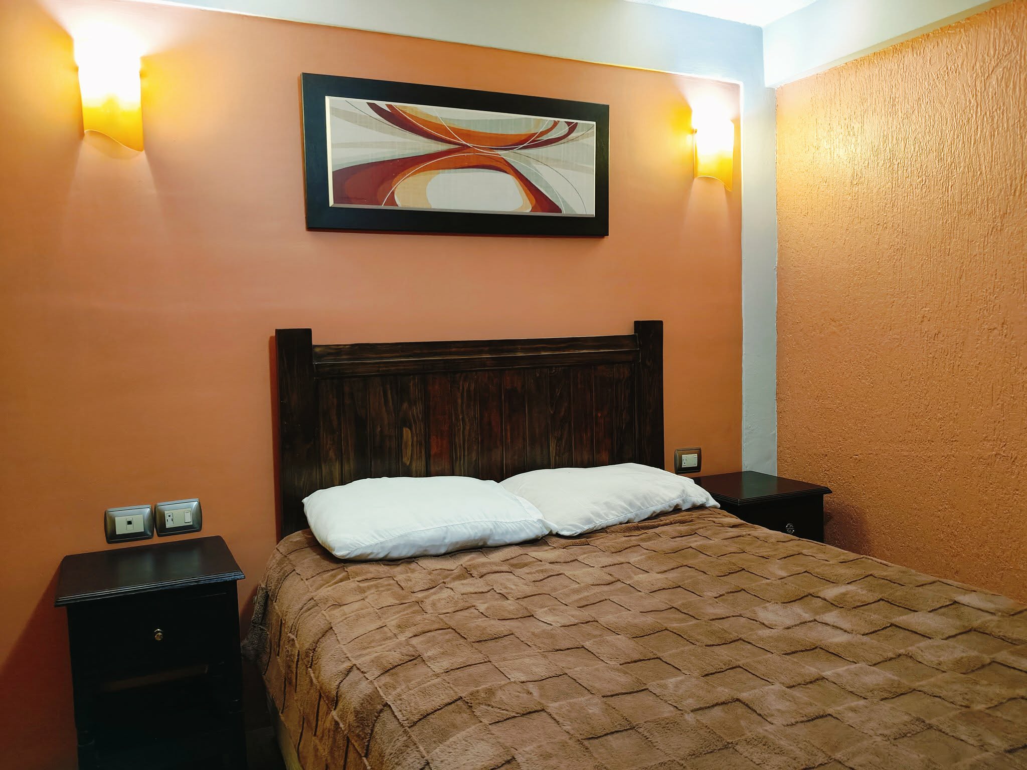 Fachada moderna del Hotel Oasis con iluminación cálida al atardecer, rodeado de árboles y vehículos en movimiento.