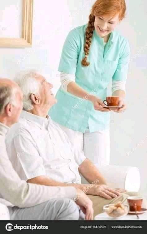 Asistente cuidando a dos personas mayores, entregando bebidas mientras sonríe.