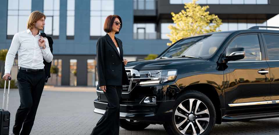 Business pair walking with luggage toward black car for airport transfer