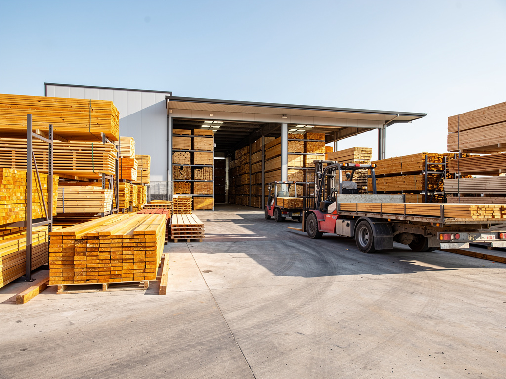 Almacén de madera con tablones apilados y carretilla elevadora cargando un camión